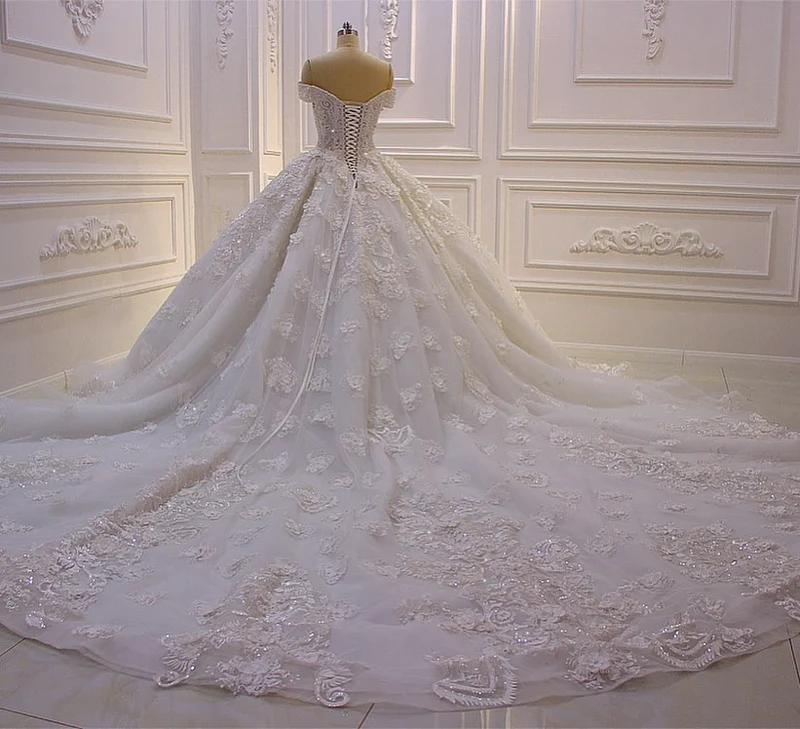 Robe de mariée élégante à épaules dénudées, coupe trapèze, manches longues, appliques et traîne.